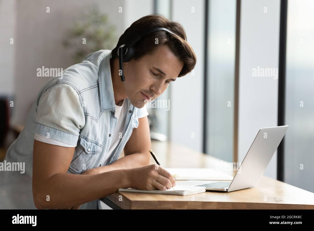Focused adult student guy wearing headphones attending virtual class Stock Photo