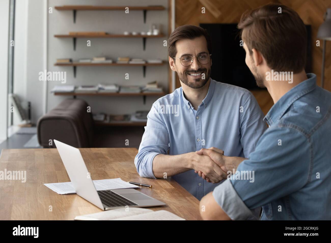 Two happy confident businessmen shaking hands at workplace Stock Photo