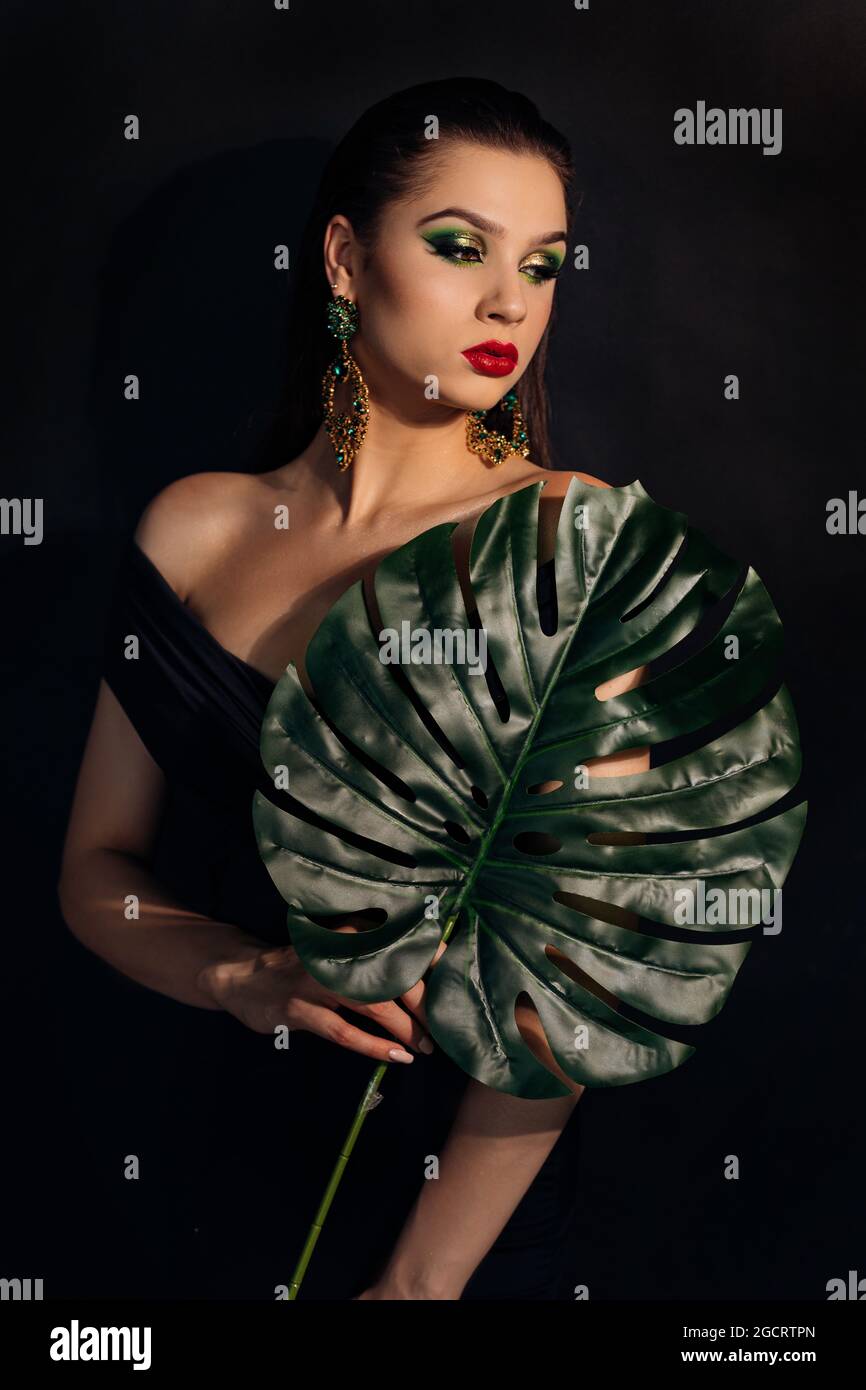 Close up face of beautiful young woman covering by green monstera green ...