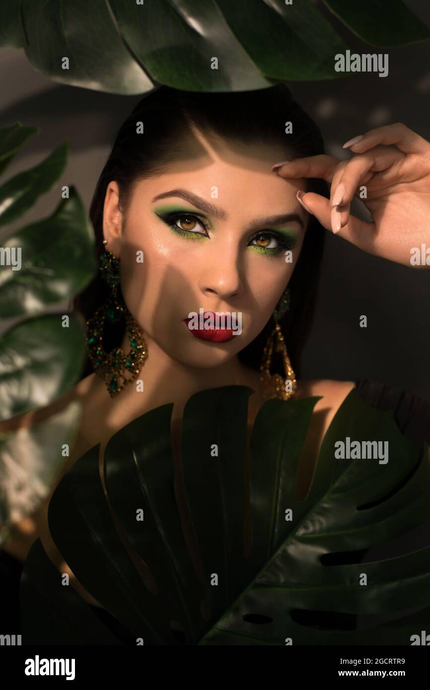 Close up face of beautiful young woman covering by green monstera green ...