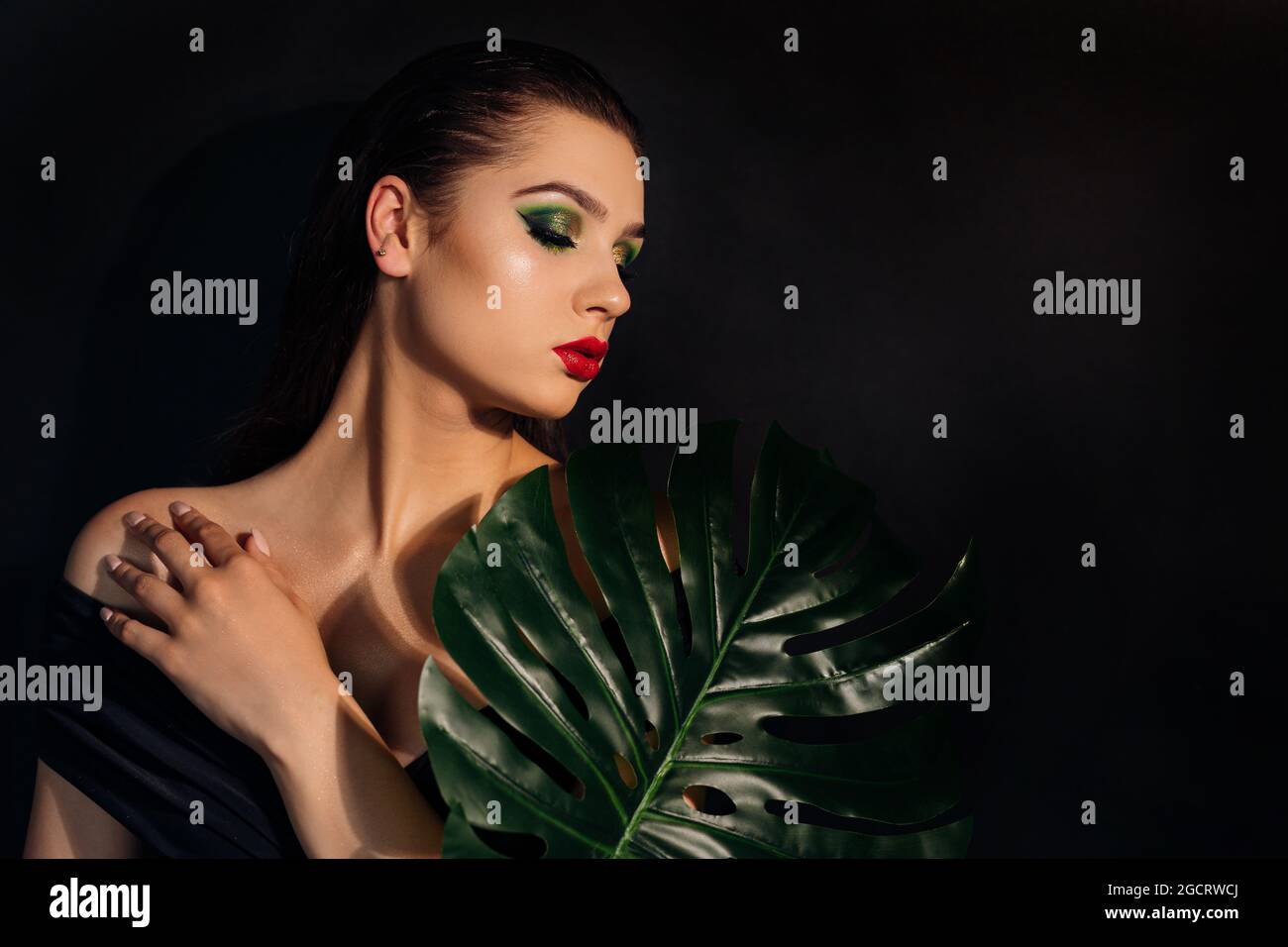 Close up face of beautiful young woman covering by green monstera green ...