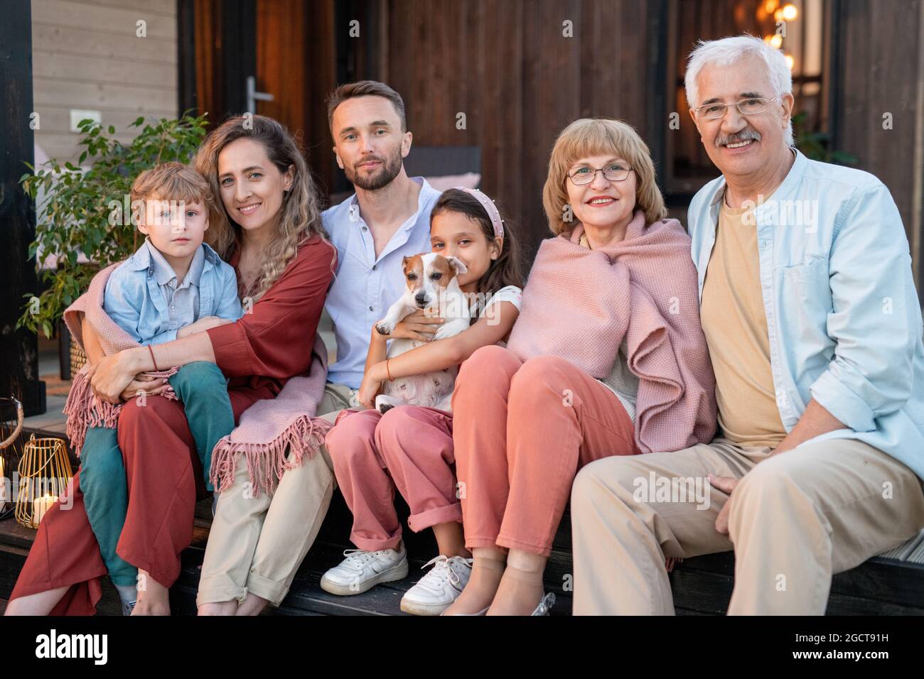 Three generations of one family sitting by their countryhouse in front of camera Stock Photo