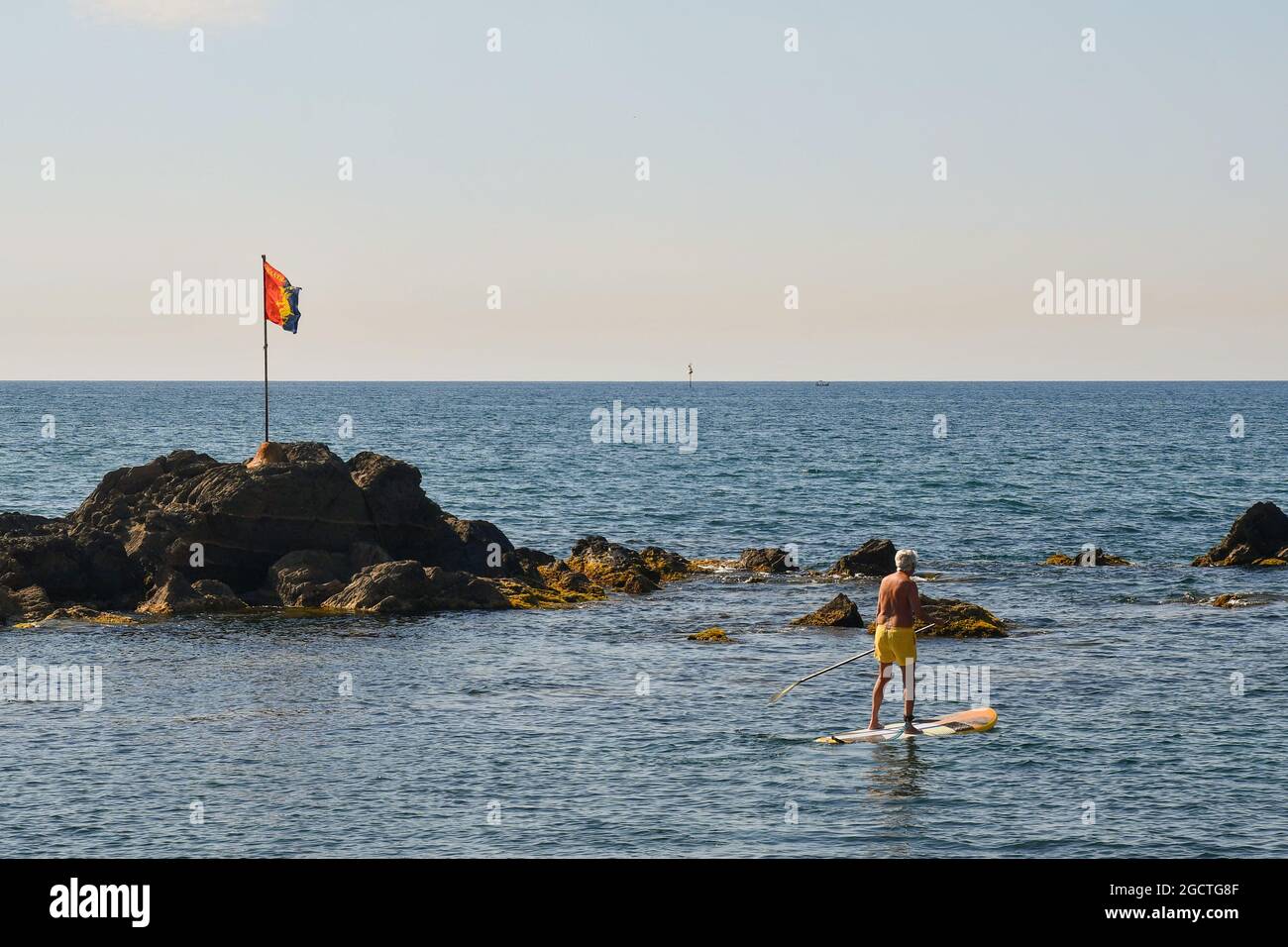 Senior man stand up paddle boarding (SUP) by the rocks on the seashore of the old fishing village Boccadasse, Genoa, Liguria, Italy Stock Photo