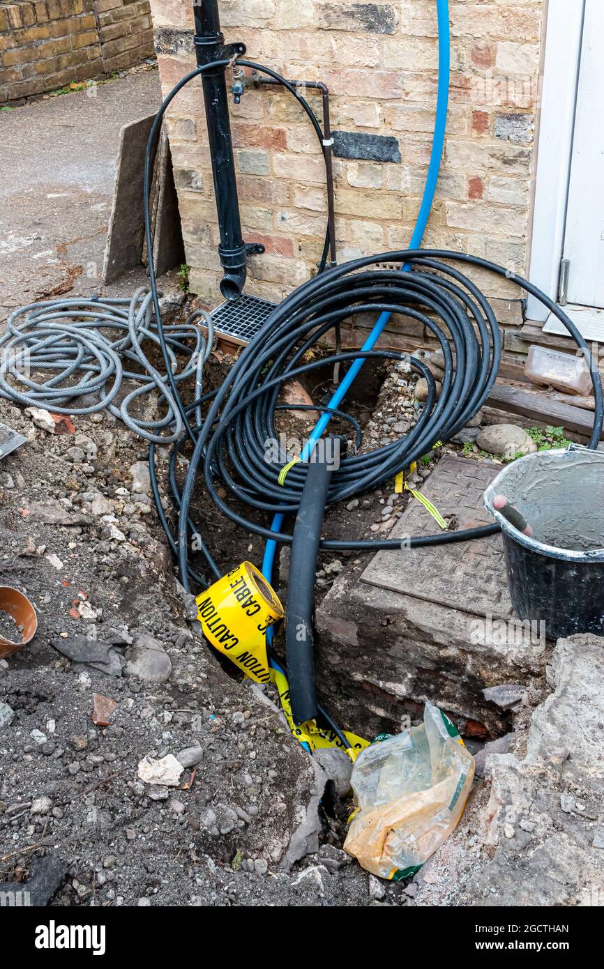 In a hole dug during construction work on a domestic property cables, pipes  and a roll of yellow Caution tape can be seen. Cambridge, UK Stock Photo -  Alamy