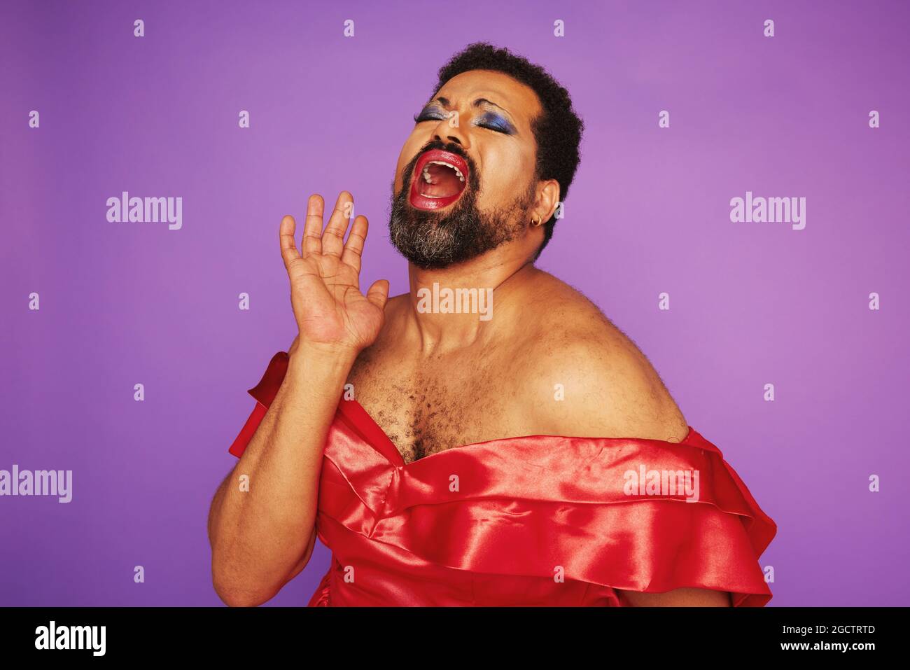 Drag queen singing in a theater. Man with beard wearing makeup and female dress giving a theatrical performance. Stock Photo