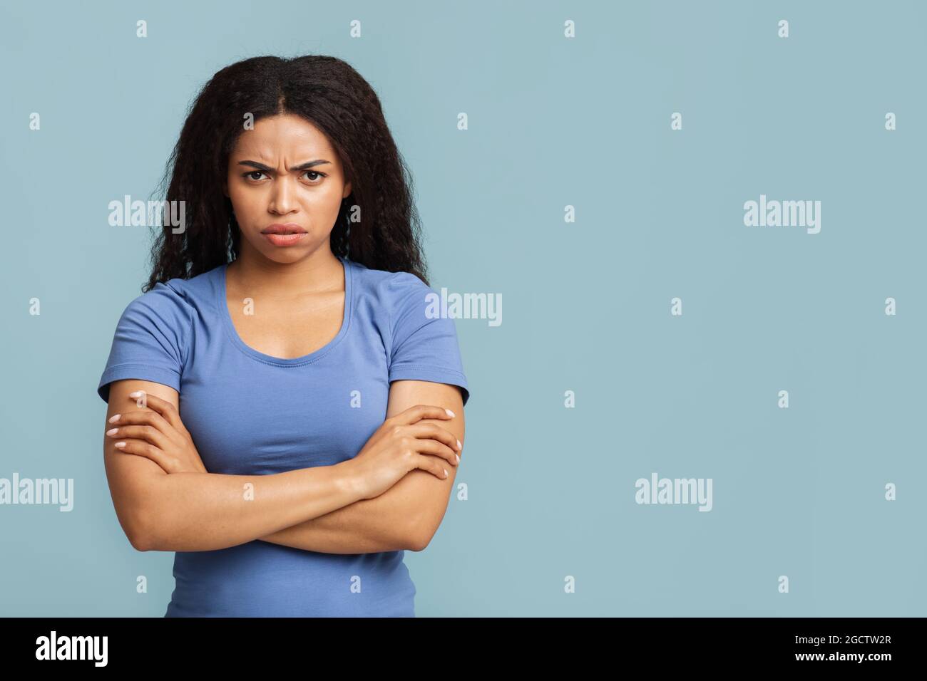 Grumpy woman. Portrait of serious black lady standing with crossed arms, posing over blue background with free space Stock Photo