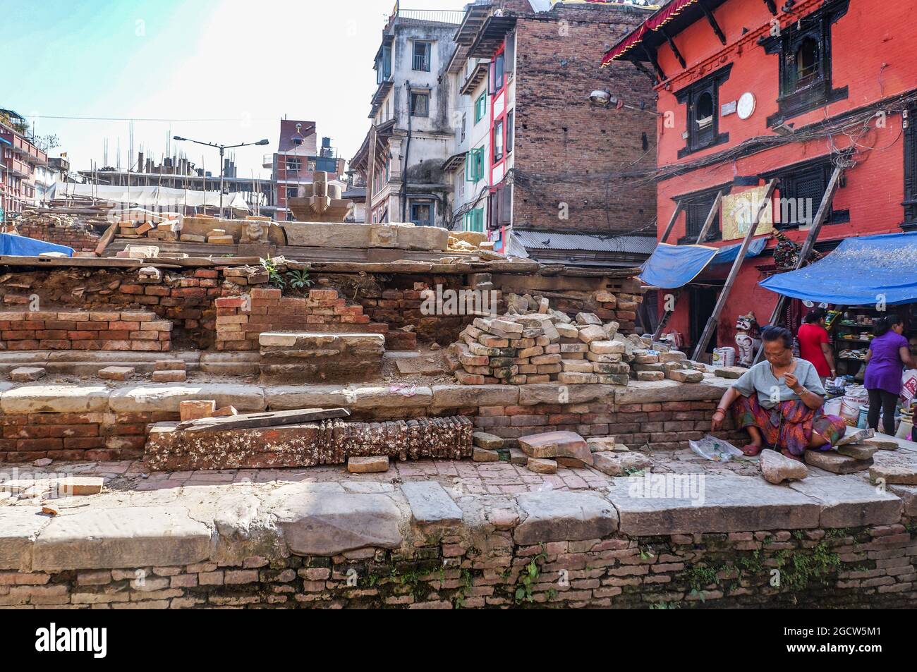 Elderly Nepalese woman sitting by the ruins of a collapsed temple, destroyed by the April 2015 Gorkha Earthquake, Kathmandu, Nepal Stock Photo