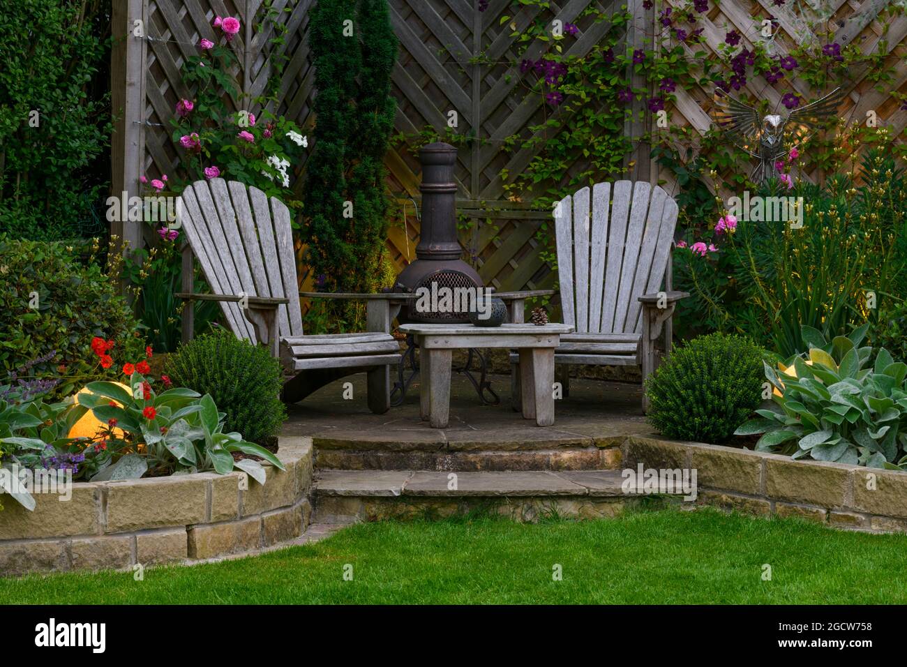 Beautiful landscaped private garden (contemporary design, mixed planting, table, seats, chiminea, illuminated globe lights) - Yorkshire, England, UK. Stock Photo