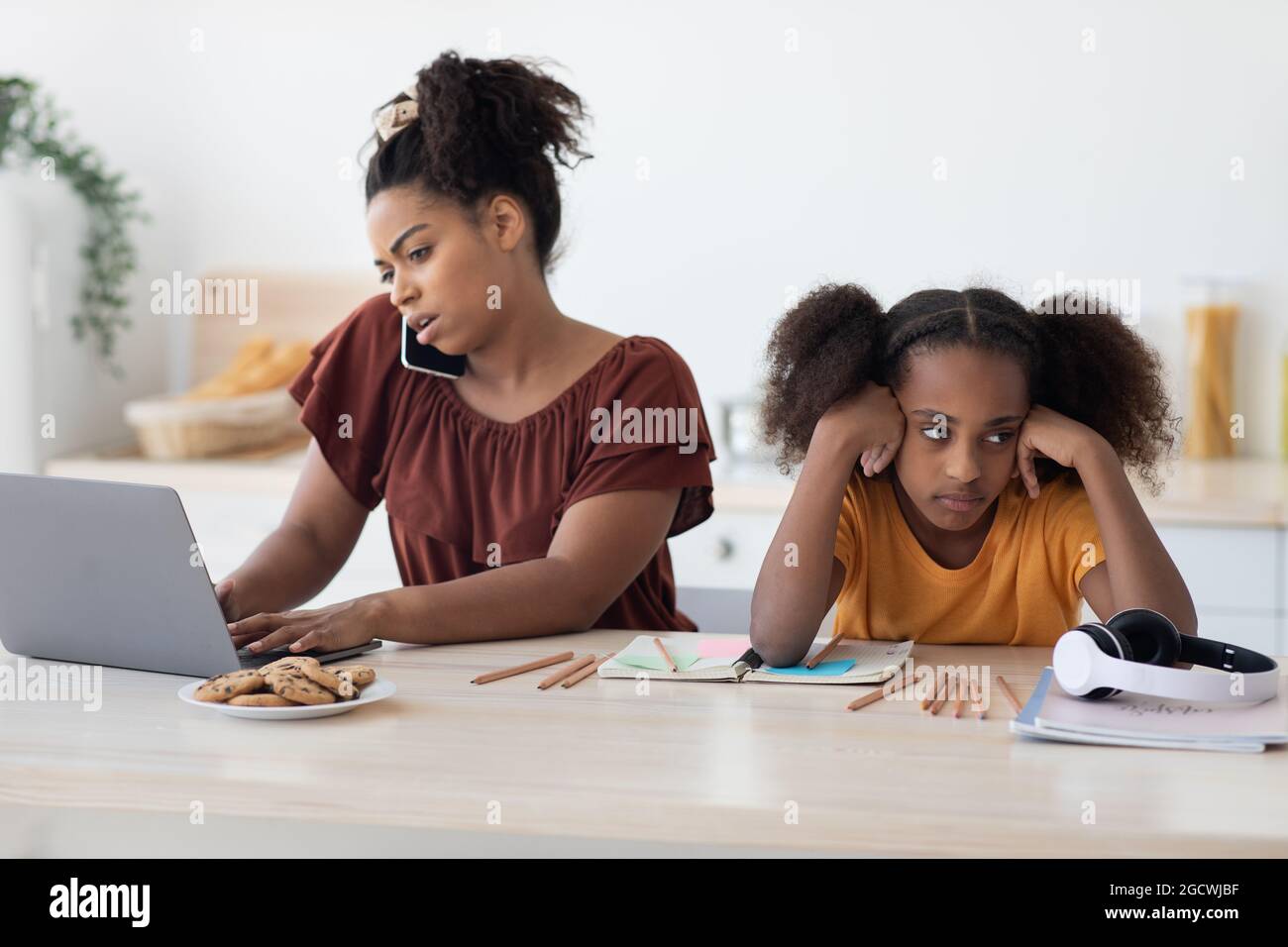 Angry teen girl sitting by working mom, kitchen interior Stock Photo