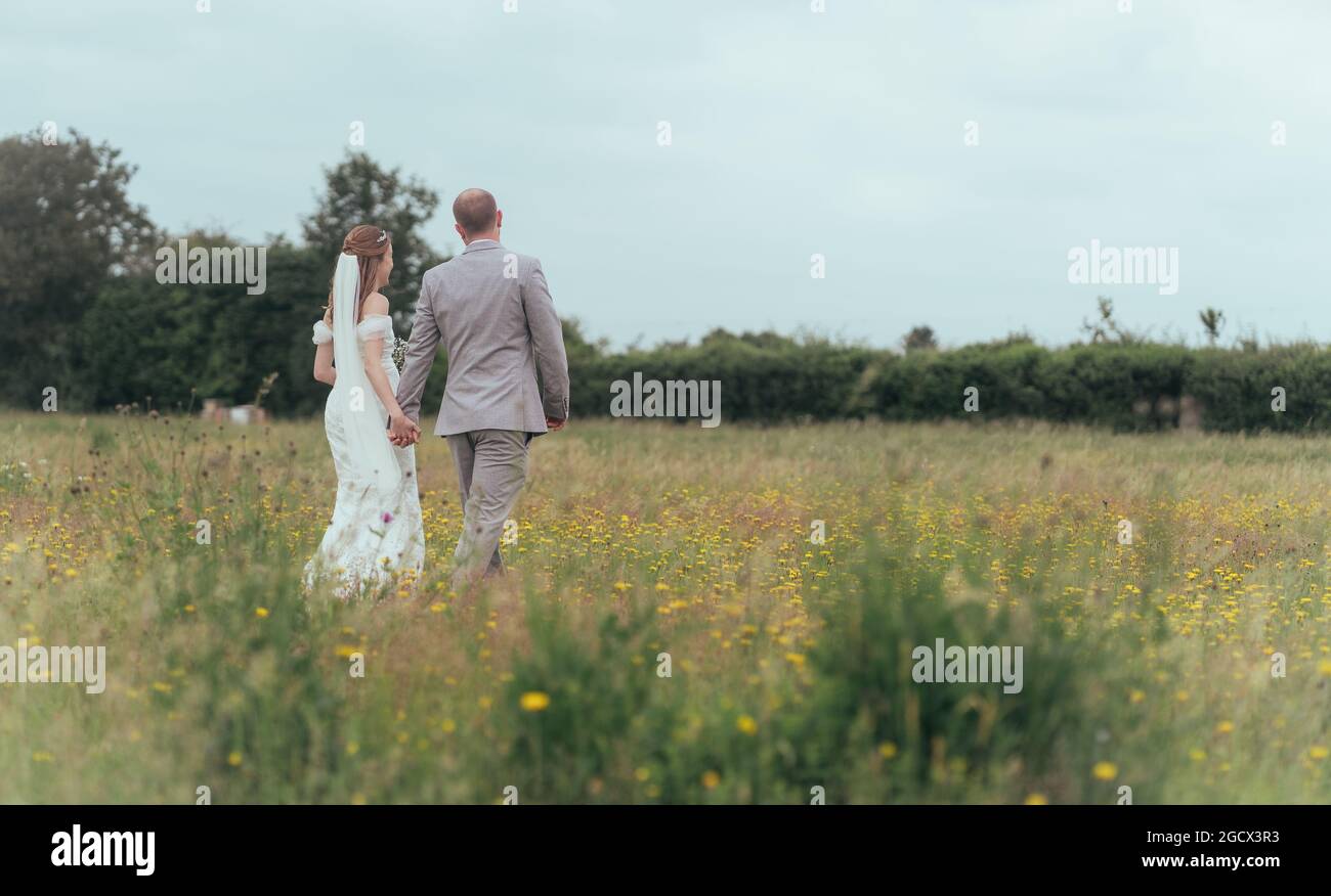 Newlywed couple wander through wild flower meadow hand in hand Stock Photo