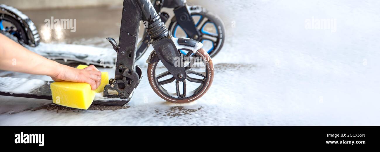 Cleaning scooter. Electric scooter care. A woman's hand washes a scooter with a sponge with foam