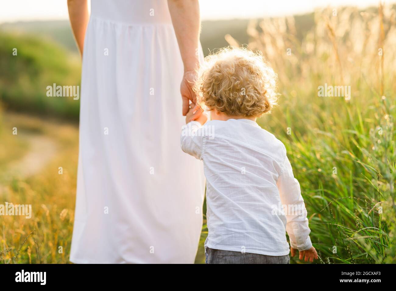 Mother leads her curly-haired son by the hand while walking in the field Stock Photo
