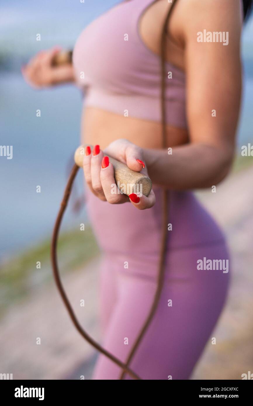Young athlete woman holding jump rope at riverbank, cardio workout, closeup Stock Photo