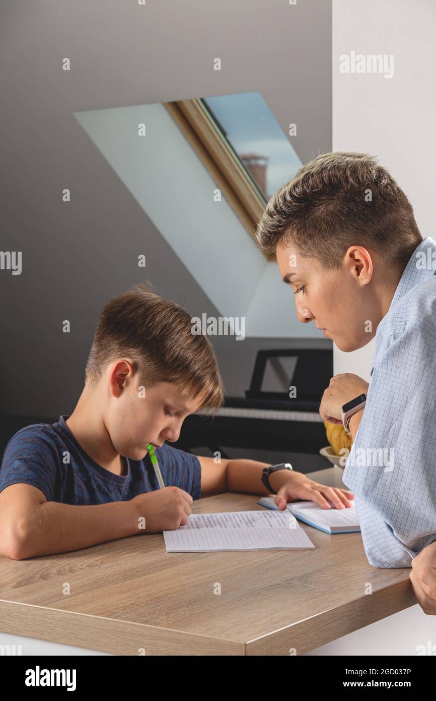 Kid boy doing homework at kitchen table with book Stock Photo
