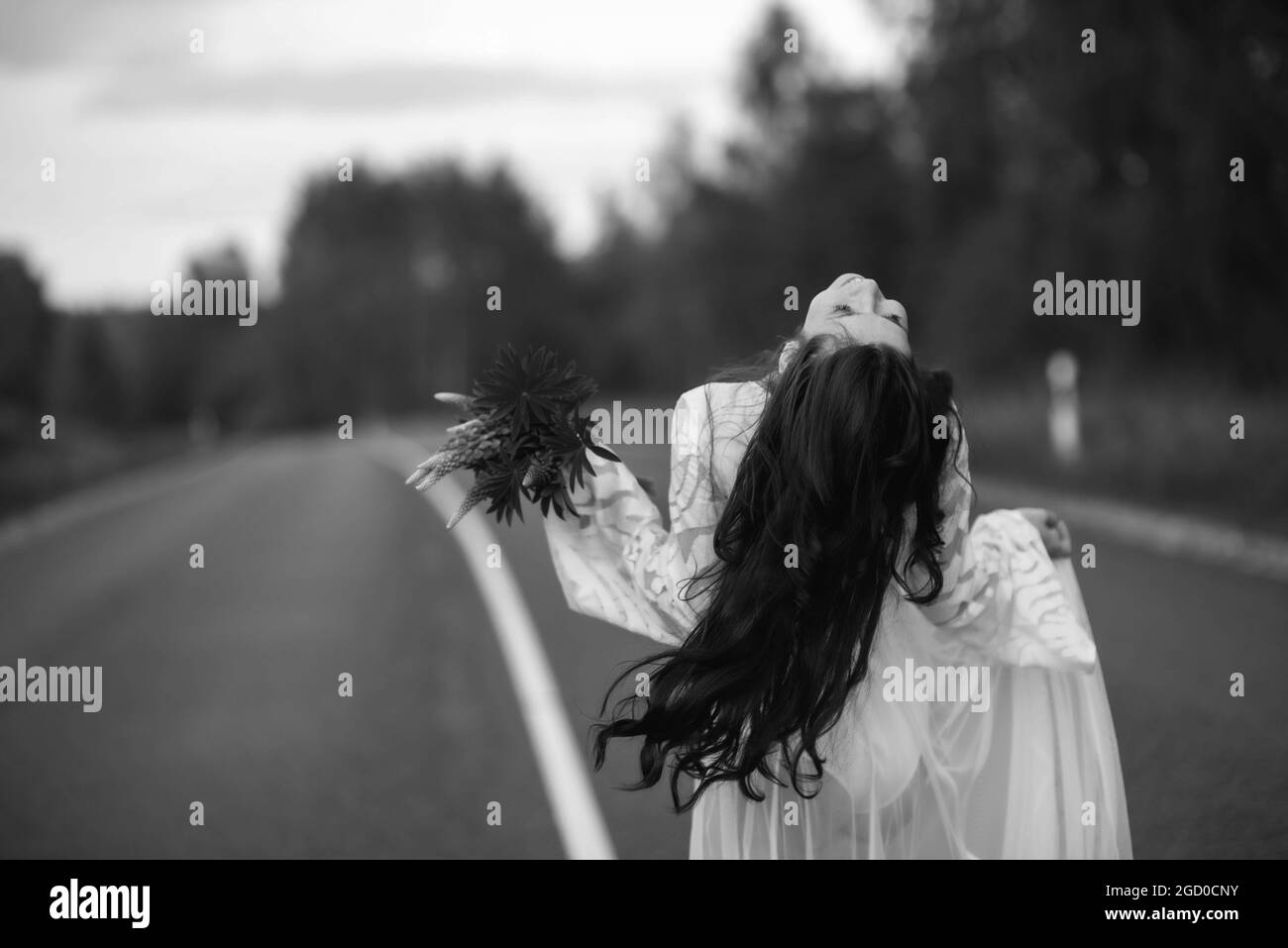 Rear view of a young woman in a white dress running on an asphalt country road Stock Photo