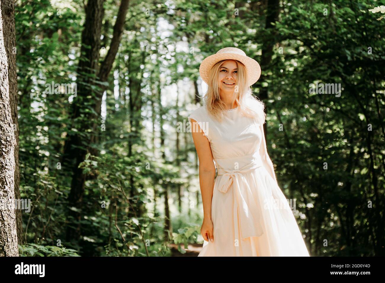 Beautiful young woman in a straw hat and white dress in a green park or ...