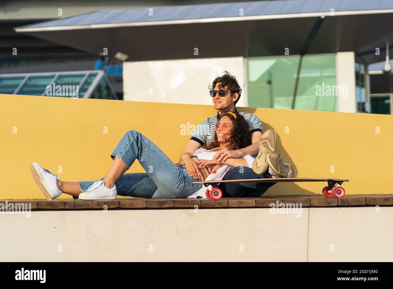 Stylish man and woman enjoy sunset cuddling at longboard relaxing after skateboarding in skate park Stock Photo