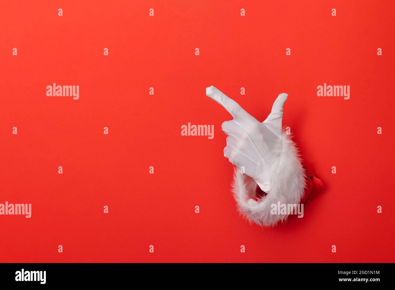 Santa Claus hand pointing through a hole in red paper background Stock Photo