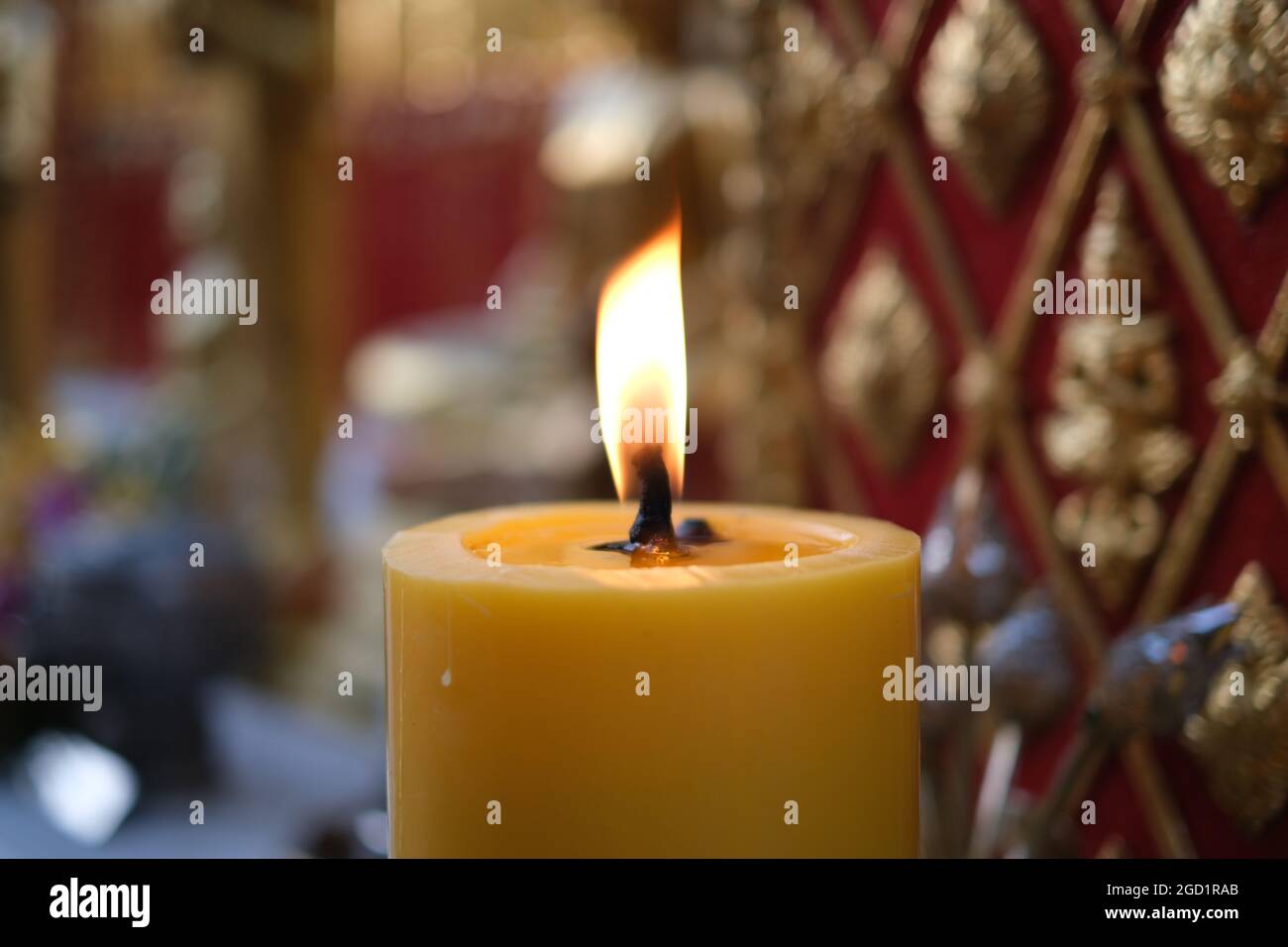 A thick lit candle against a backdrop of religious symbols in a Buddhist temple at north of Thailand Stock Photo