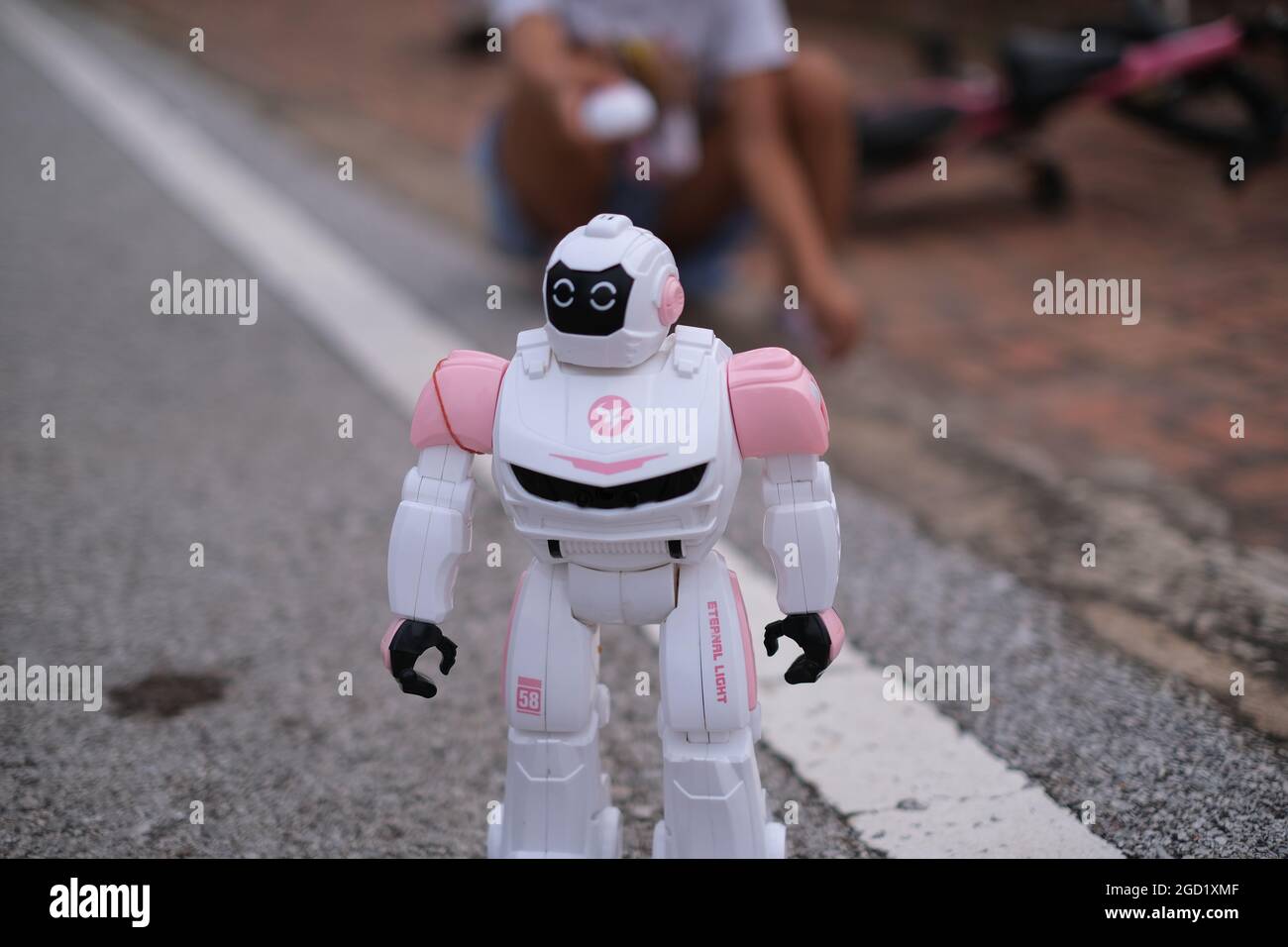 A toy robot, radiocontrolled by a girl, is moving over the roadway
