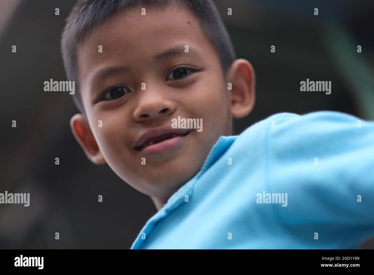 Cute yet naughty 7-years old Thai boy is looking downward straight to the camera Stock Photo