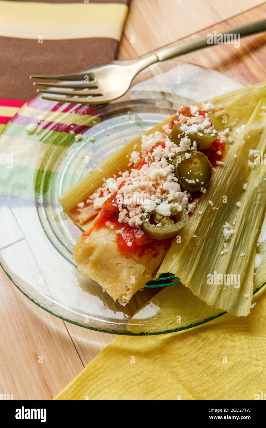 Mexican steamed chili and cheese masa tamales wrapped in corn husk topped with spicy tomato salsa and queso fresco crumbles Stock Photo