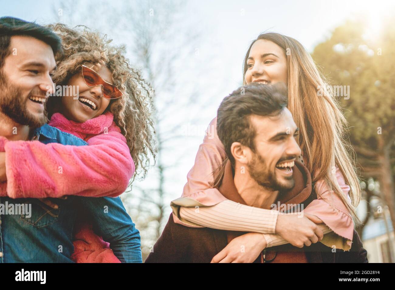 Interracial happy friends laughing having fun piggybacking outdoors - concept of young people friendship. Stock Photo