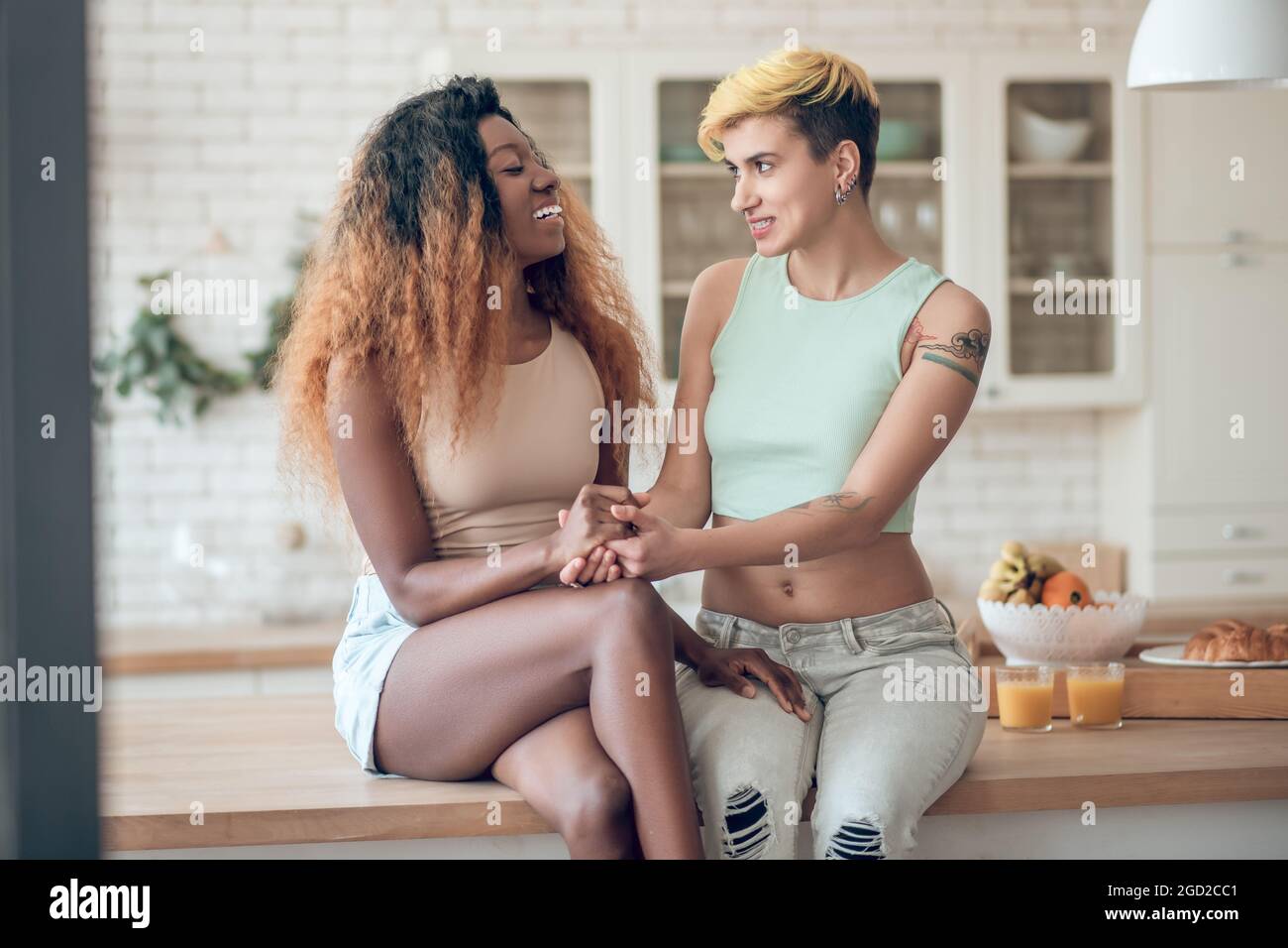 Two female friends holding hands sitting on table Stock Photo