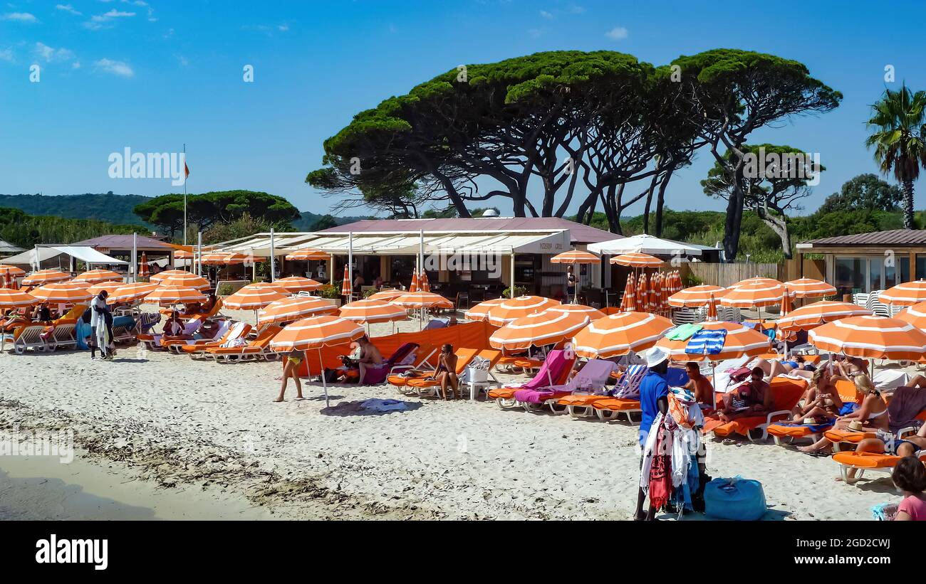 St. Tropez (Tahiti plage), France - June 9. 2016: View on crowded sand beach with many umbrellas and sunbeds, mediterranean pine trees background agai Stock Photo