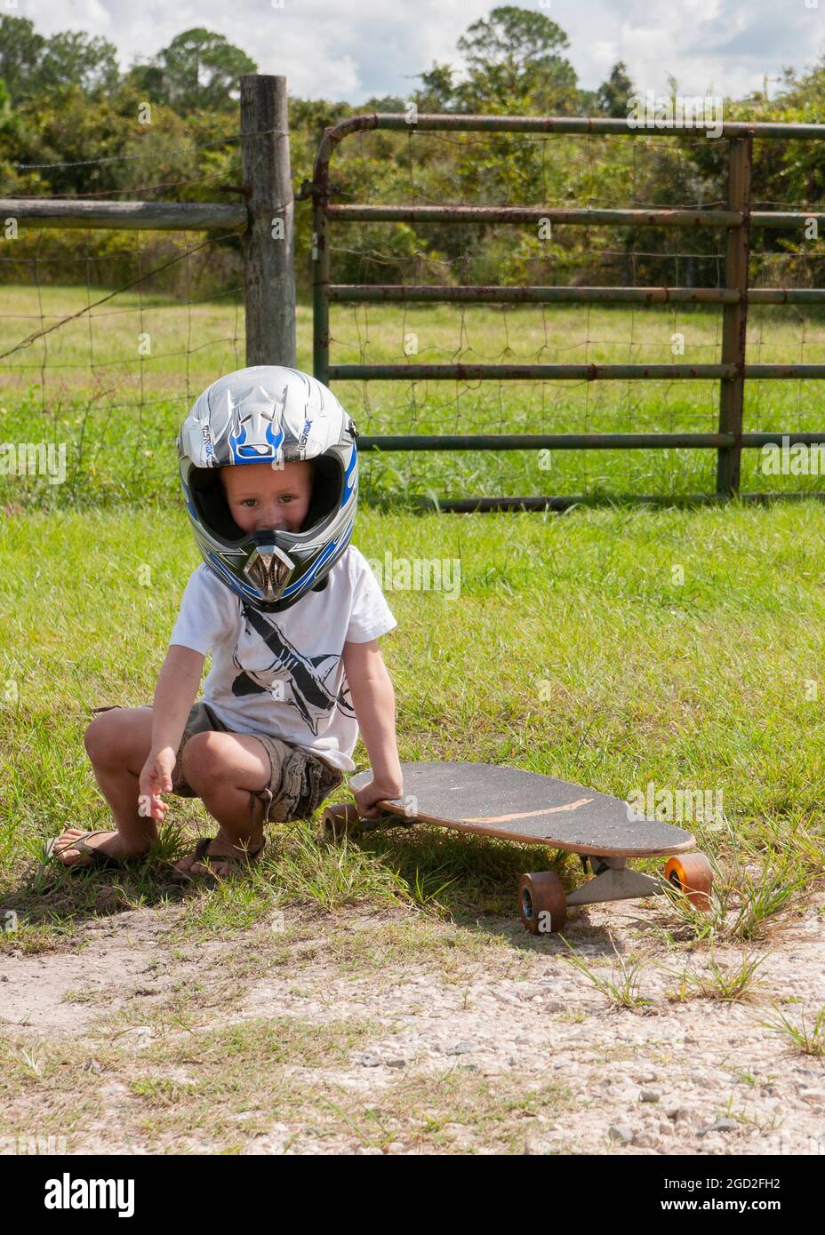 Young boy with long skateboard on gravel driveway wearing a motorcycle