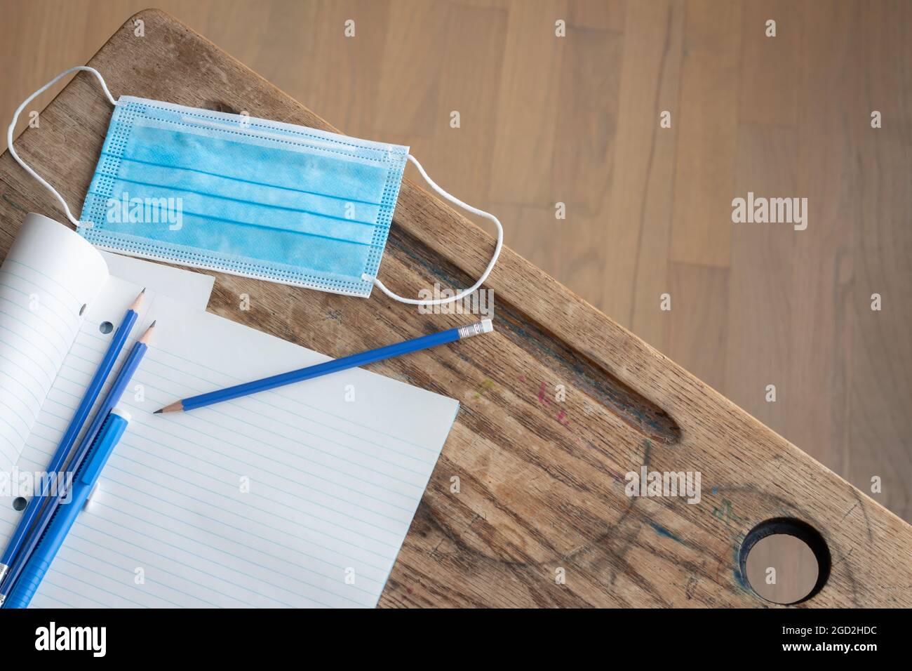 blue disposable face mask with open notebook to blank white page and blue pencil on vintage wood desk with copy space Stock Photo