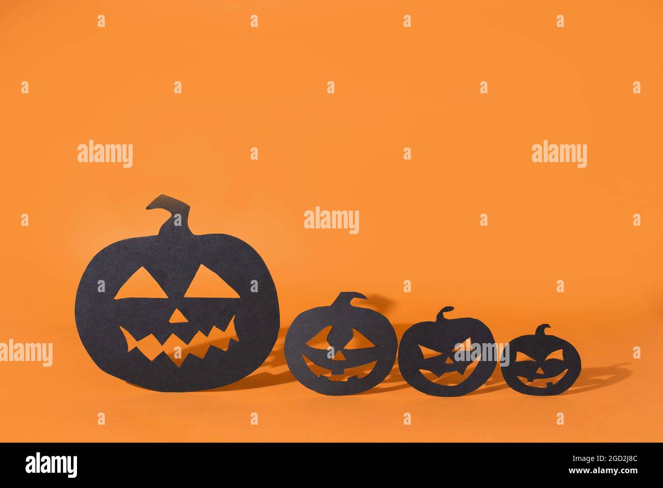 Four paper pumpkins with carved faces casting shadow on orange ...