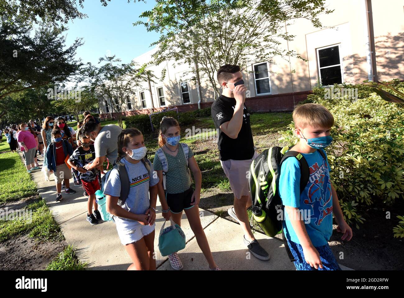 Orlando, United States. 10th Aug, 2021. Students wearing face masks arrive with their parents on the first day of classes for the 2021-22 school year at Baldwin Park Elementary School. Due to the current surge in COVID-19 cases in Florida, Orange County public schools have implemented a face mask mandate for students for 30 days unless a parent chooses to opt out of the requirement. Credit: SOPA Images Limited/Alamy Live News Stock Photo