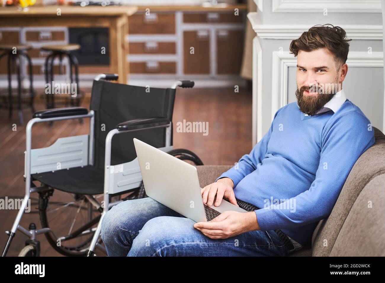 Disabled man sitting on a comfy couch and using a laptop Stock Photo