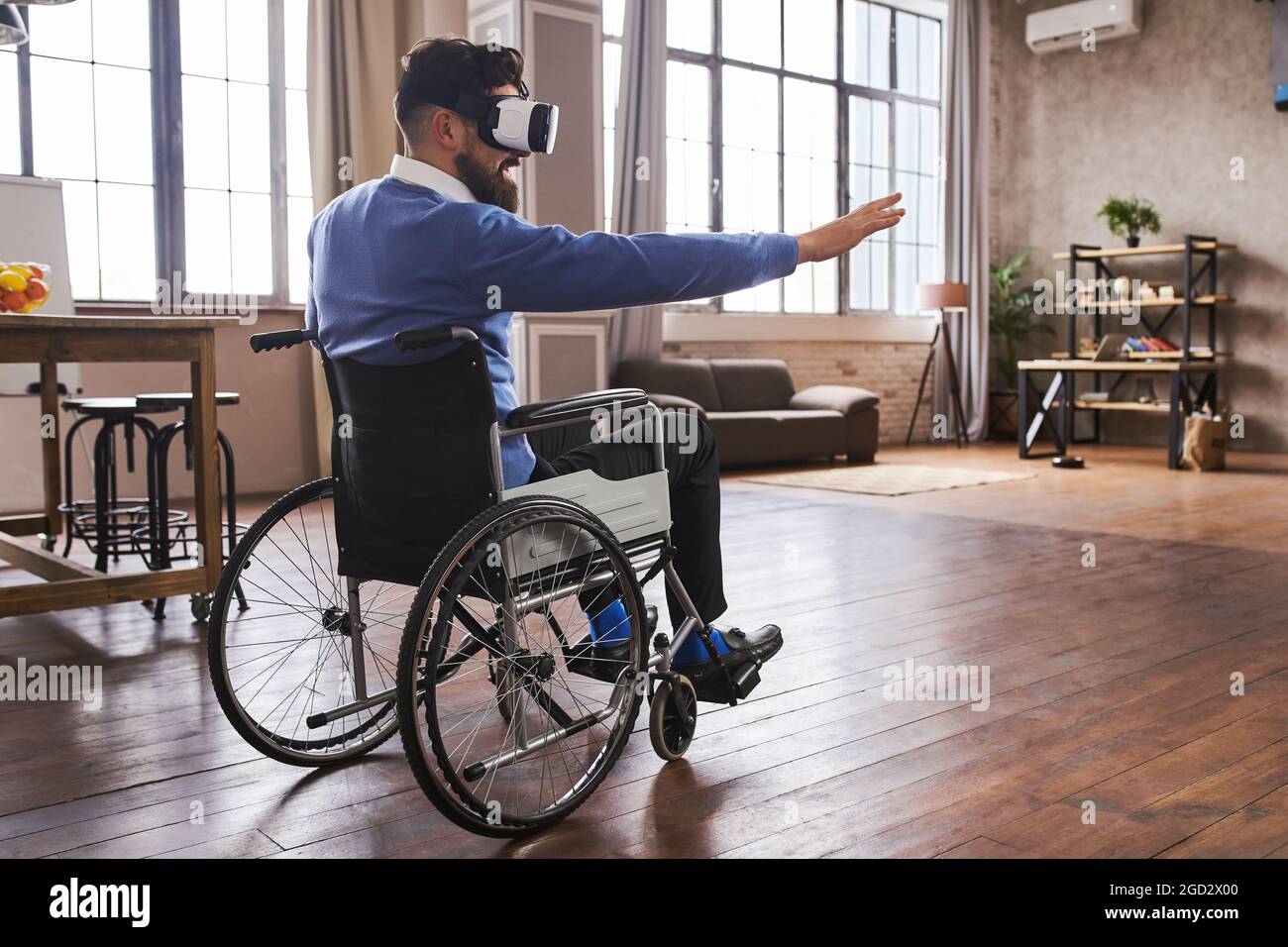Man in a wheelchair using a VR headset and trying to touch virtual objects Stock Photo