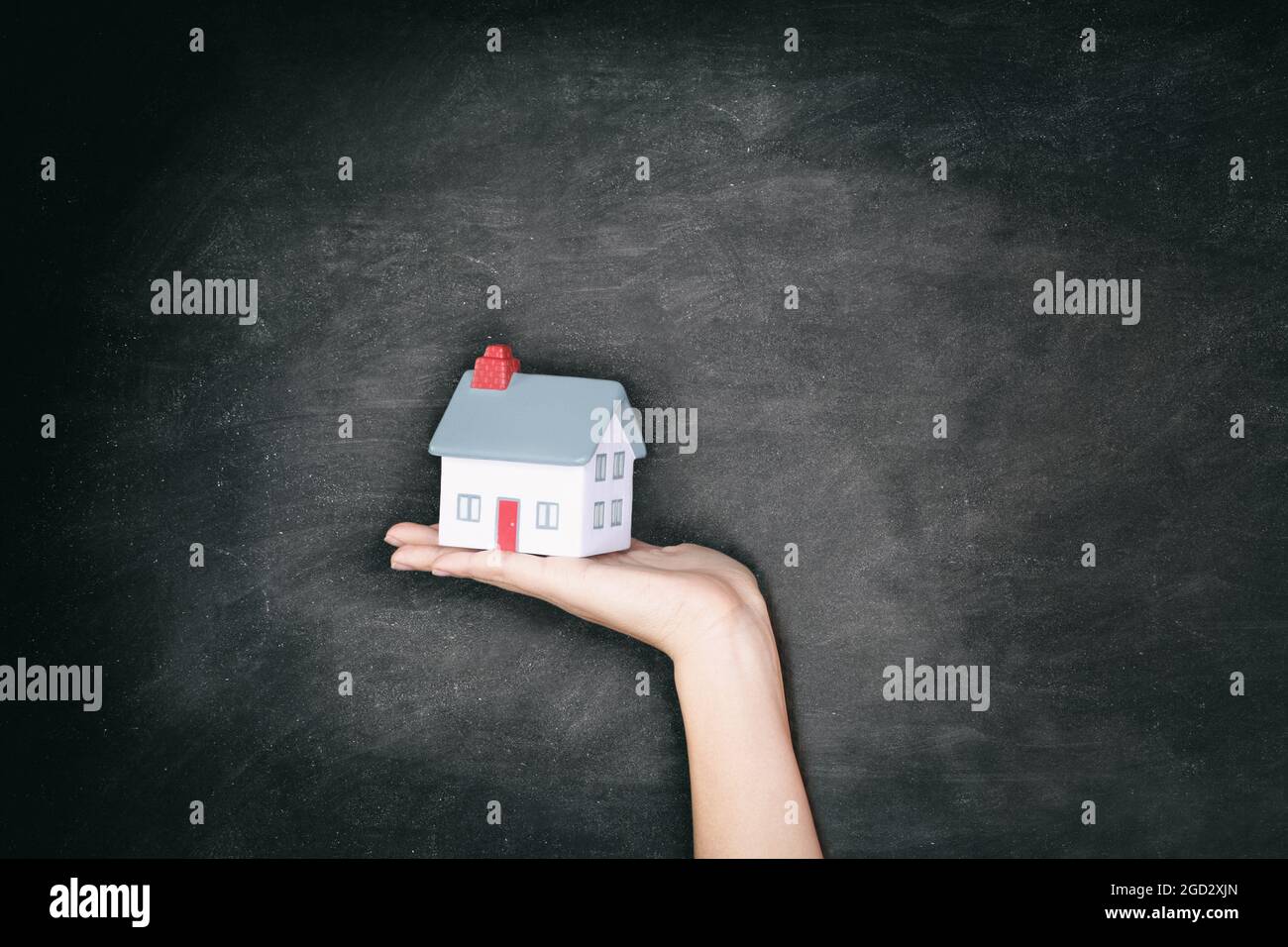 Real Estate blackboard background - New home ownership woman showing miniature house toy for homeowner concept billboard. Stock Photo