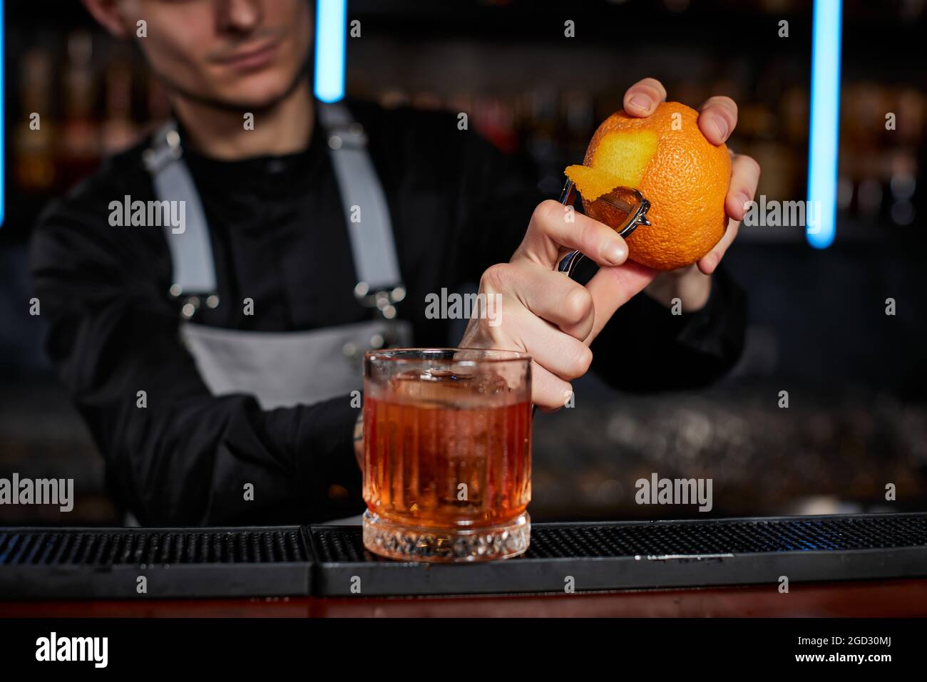 Bartender peels orange peel for cocktail at bar Stock Photo by