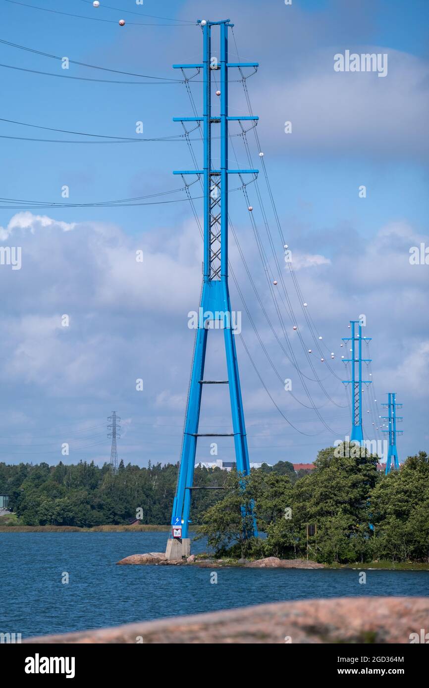 Helsinki / Finland - AUGUST 10, 2021: A line of modern high voltage electricity pylons on the shore against cloudy sky. Stock Photo