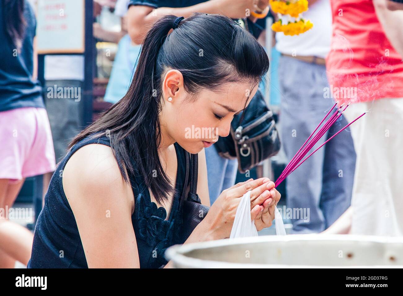 Attractive Thai female holding incense sticks whilst praying at Erawan Shrine, Bangkok, Thailand