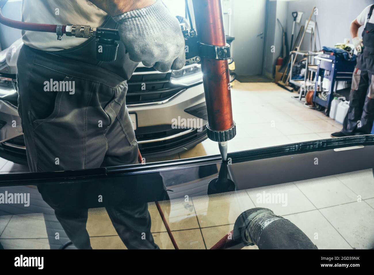 Install auto windscreen on car process. Service man applies glue using special equipment to new