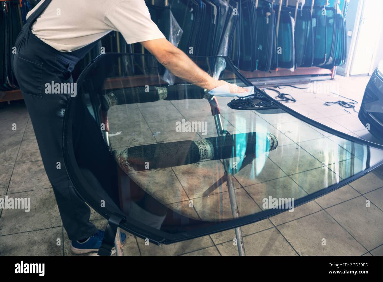 Automobile glazier worker degreases glass windscreen or windshield before installation on car in service station garage. Stock Photo