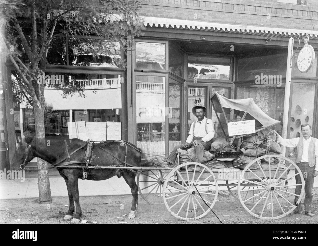 Man sitting in a horse drawn wagon in front of a store ca. between 1909 and 1923 Stock Photo