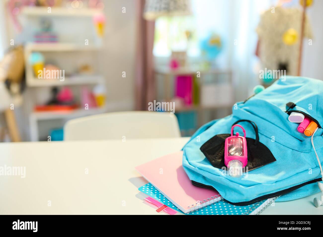 Back to school. Closeup on white table with workbooks, stationary, backpack, ffp2 mask and antiseptic at student room in sunny day. Stock Photo