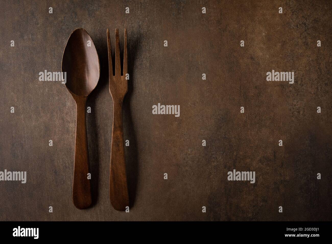 A rustic brown textured background with dark wood fork and spoon serving utensils Stock Photo