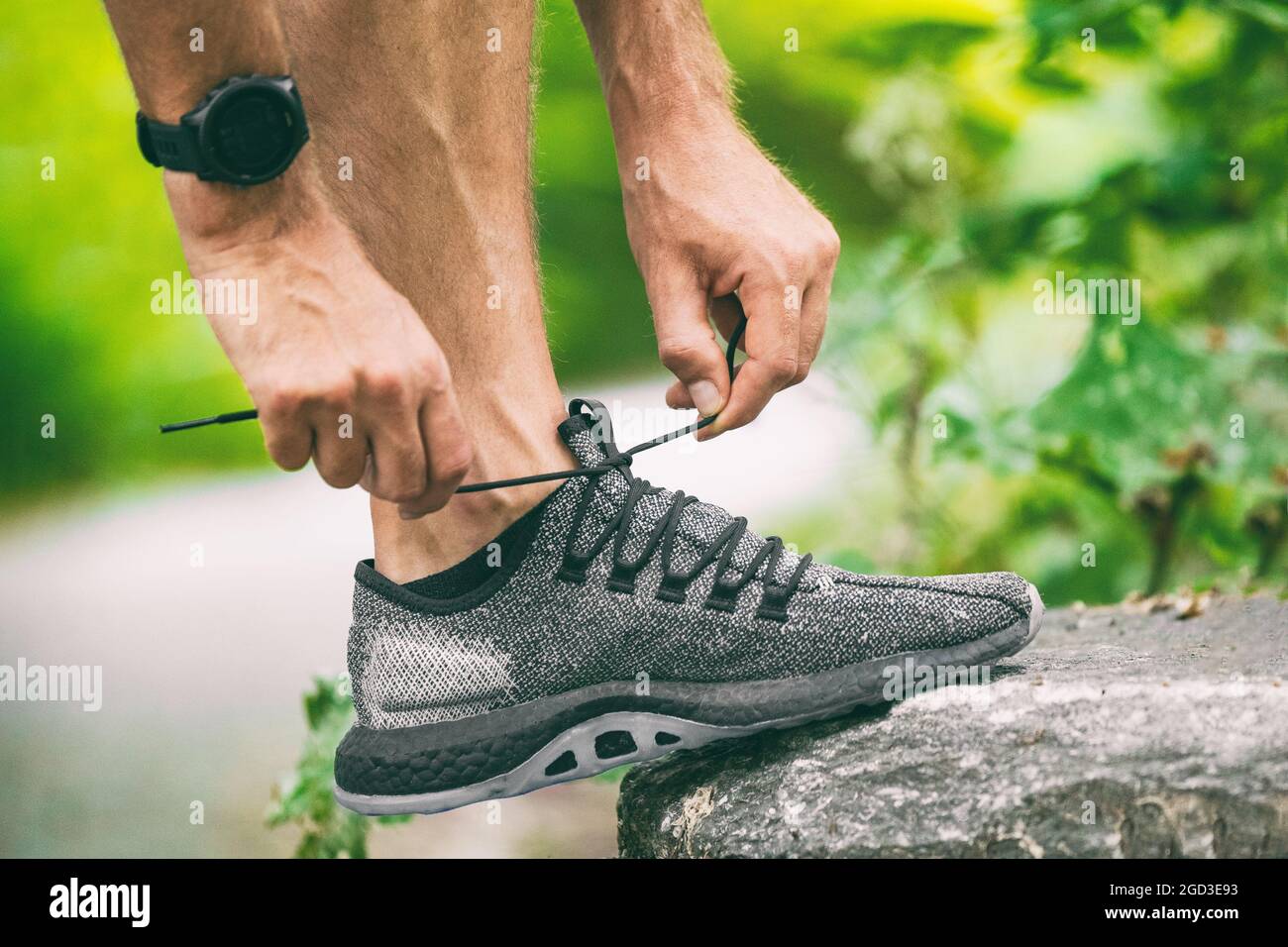 Exercise wearing heart rate tracker smartwatch sports watch man getting ready to run or walk outside lacing running shoes. Contact tracing with app Stock Photo