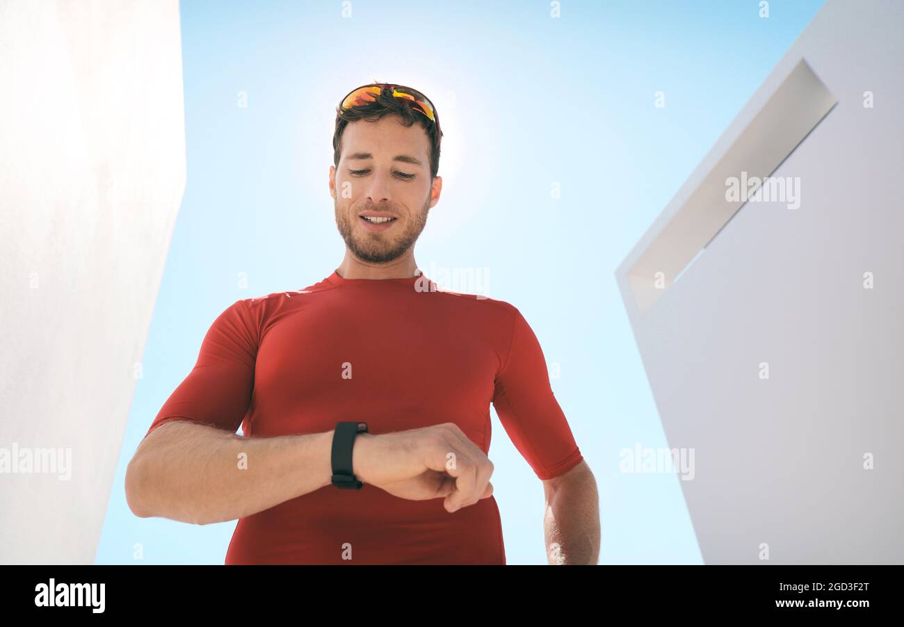 Sports watch athlete man running checking his wearable technology smartwatch heart rate monitor during outdoor workout at home or gym. Stock Photo