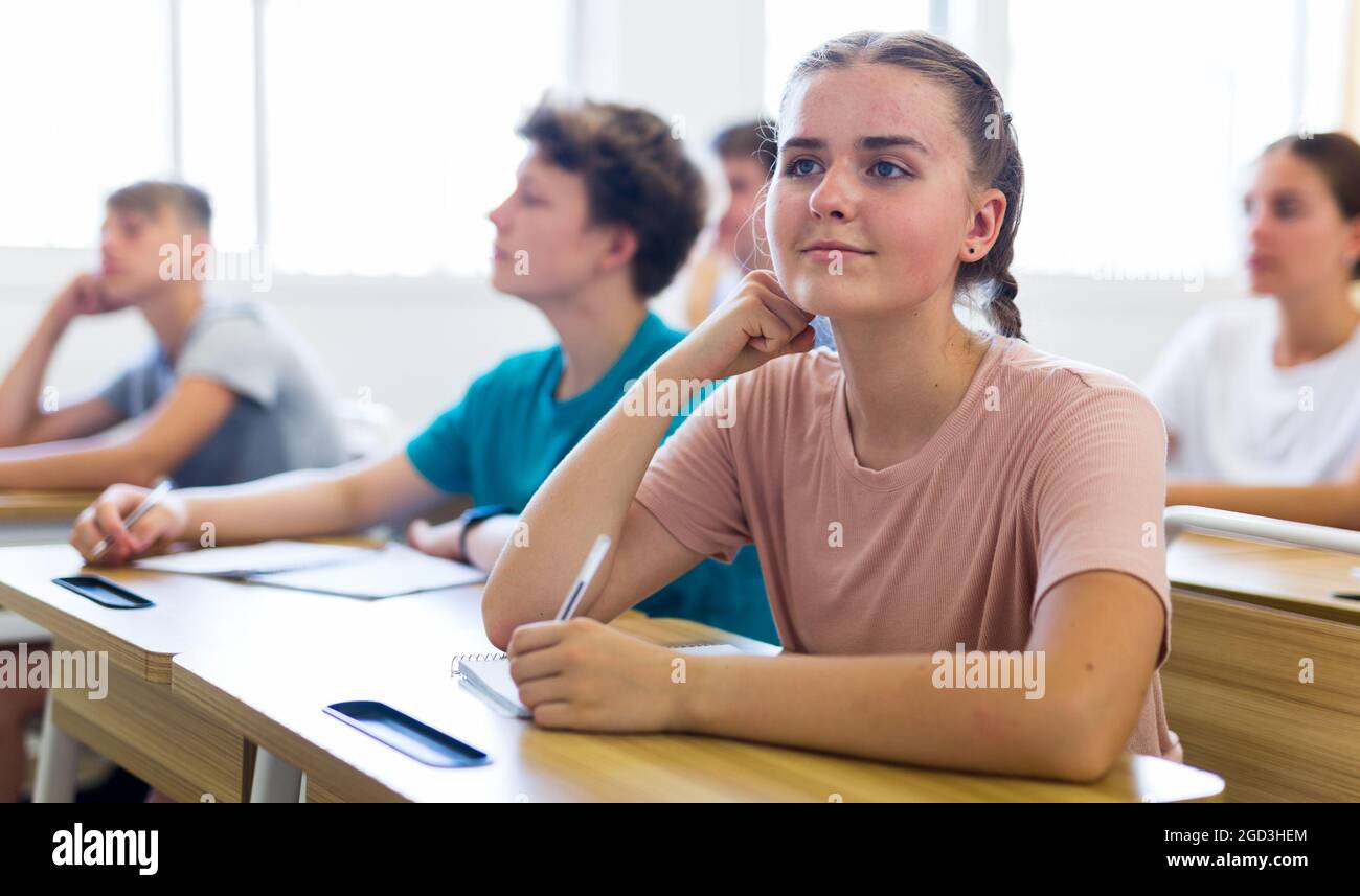 Dreamy teenage girl sitting at school desk during lesson Stock Photo ...