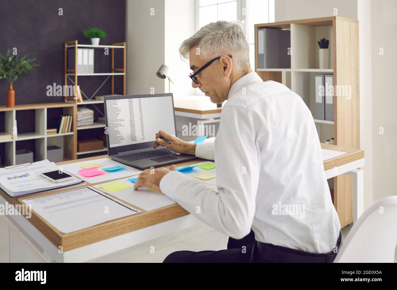 Senior man working at office desk with papers, post-it notes and laptop computer Stock Photo