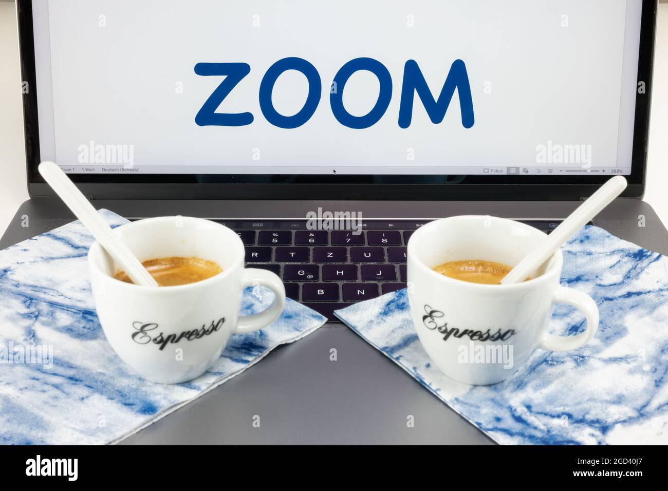 Two coffee cups lie on a desktop computer, and the screen says Zoom
