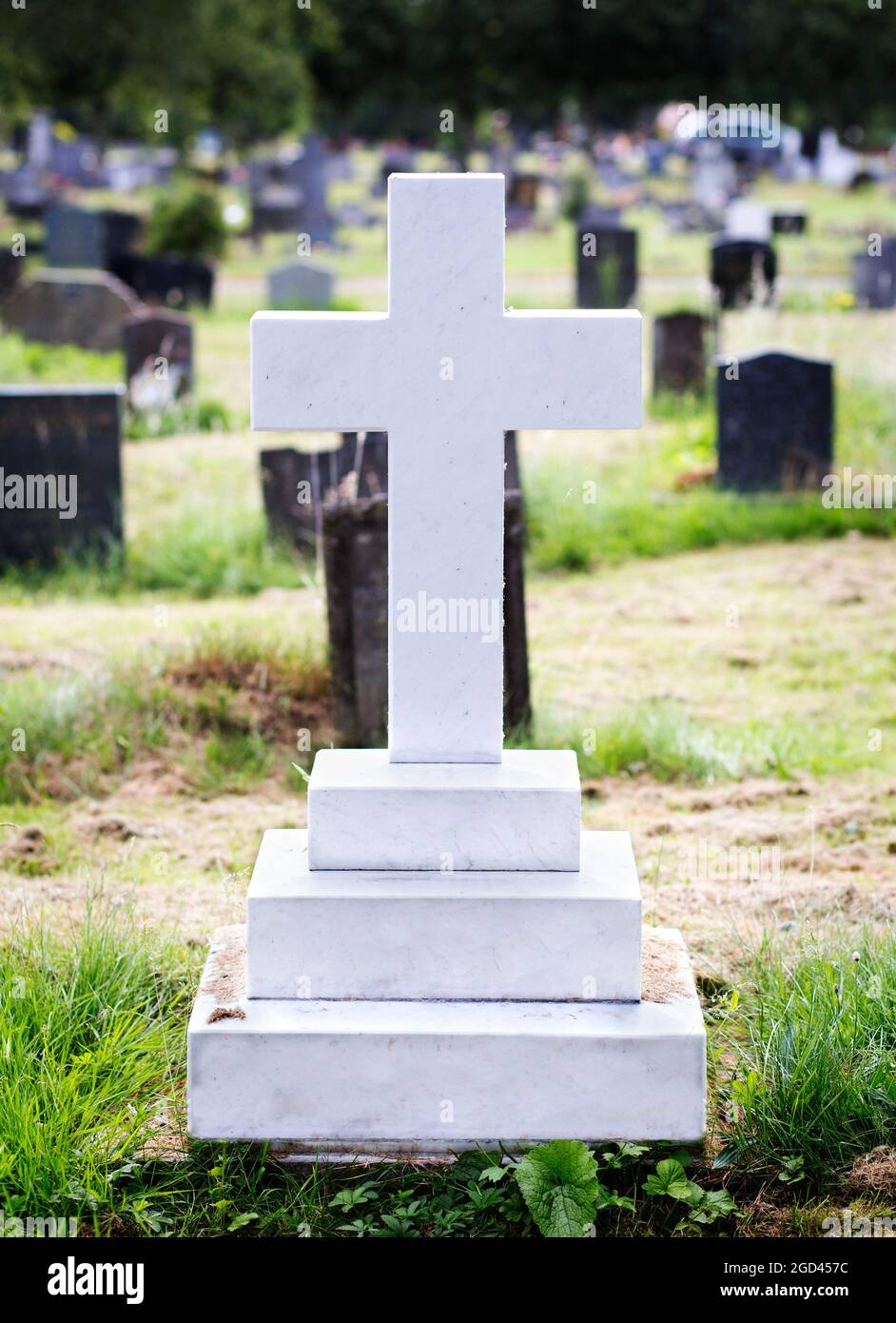 White marble gravestone (blank) in the shape of a cross. Trees and